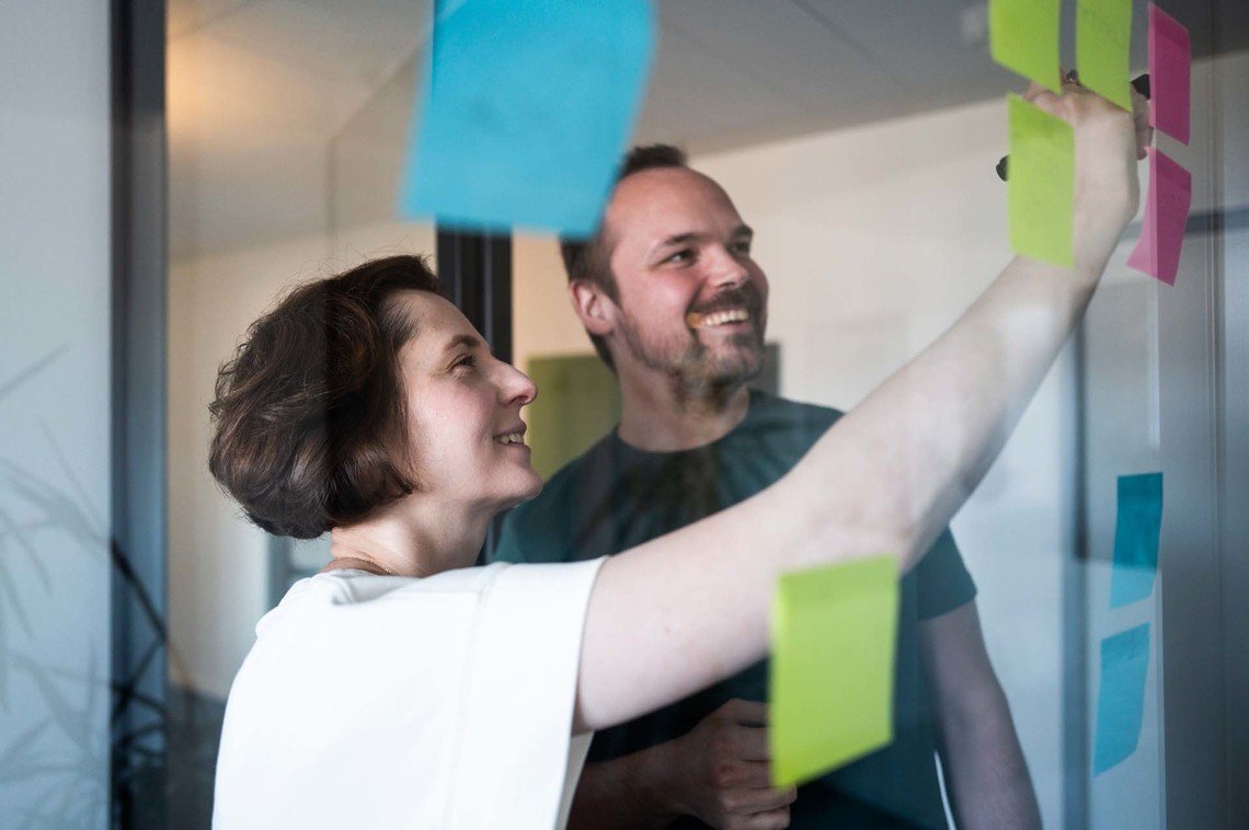 Zwei Mitarbeiter:innen der Digitalagentur mindshape brainstormen mit Post-its an einer Glastür
